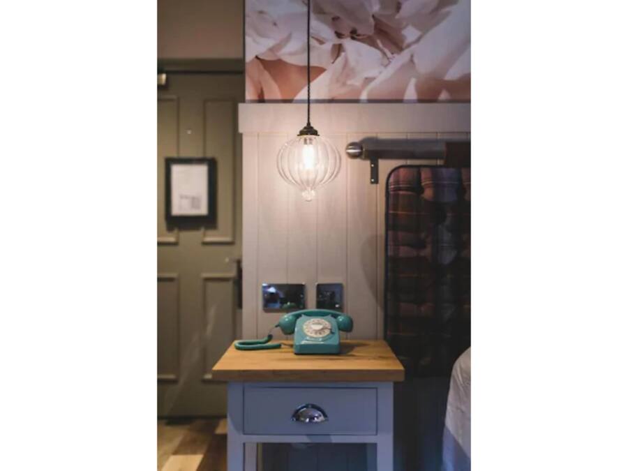 A vintage-style telephone on a wooden table with a drawer below, a wall-mounted light fixture, and a framed picture above.