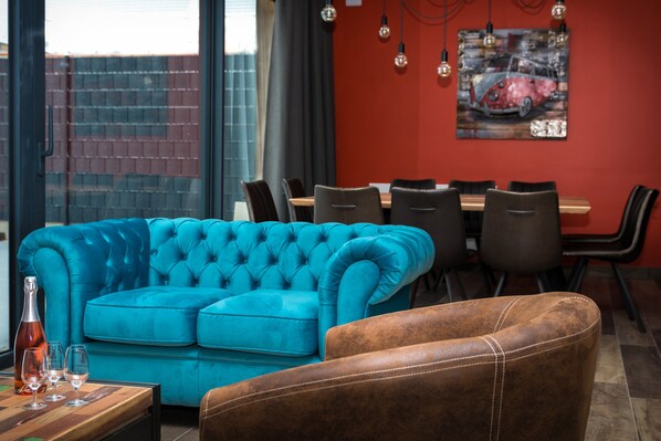 A modern living room with a blue sofa, a brown leather chair, a dining table with chairs, and a painting on the wall. - L'Attrap'Reves (Ergersheim)