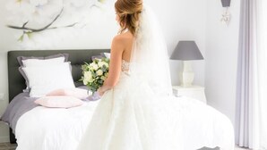 A bridal suite with a large bed, a nightstand, a lamp, and a wall with a floral painting. - L'Attrap'Reves (Ergersheim)