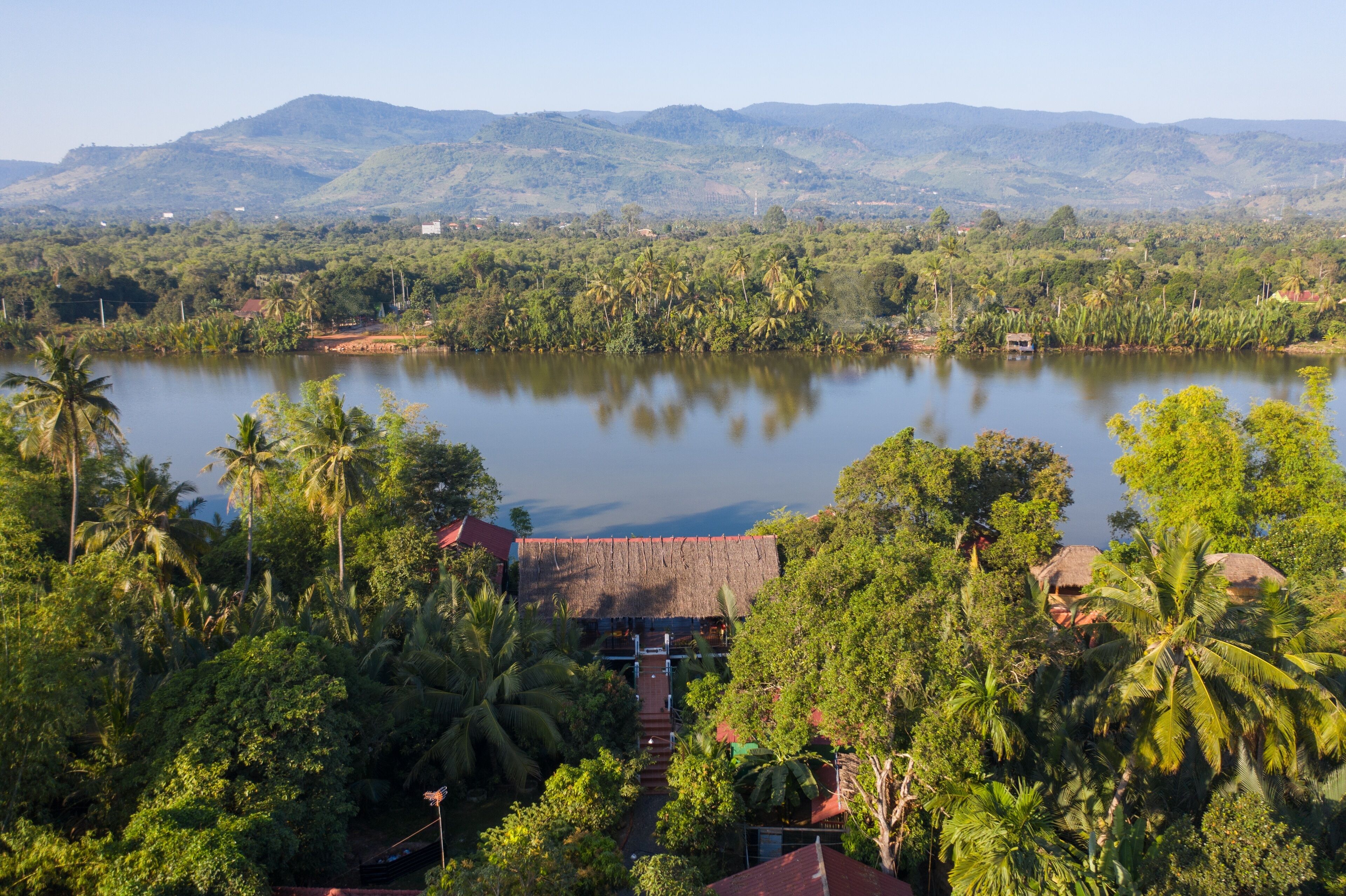 A tropical resort with a thatched-roof building surrounded by lush greenery and a lake.
