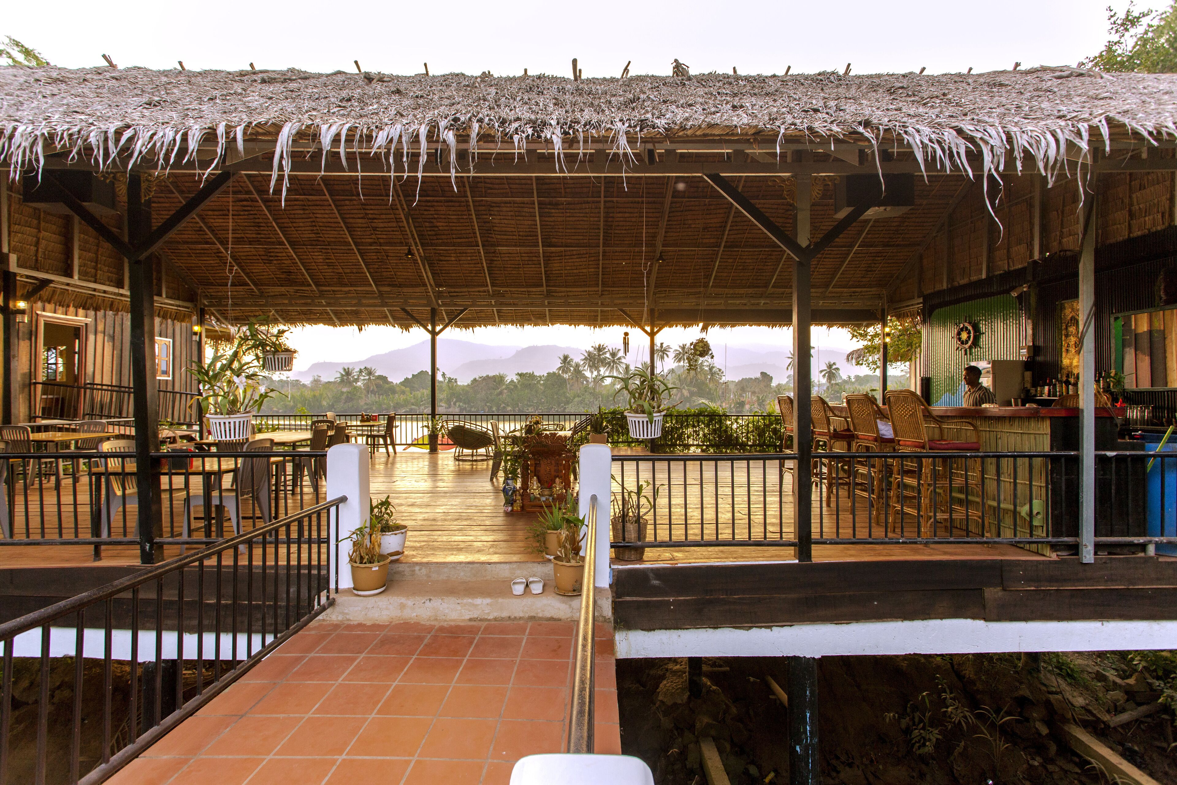A covered outdoor seating area with chairs and tables, potted plants, and a view of the surrounding landscape.