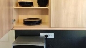 Una cocina con armarios de madera, un microondas y tazones negros en estantes.