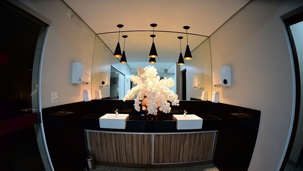 A modern bathroom with a curved vanity, black countertops, and a central floral arrangement. - Topazio Imperial Hotel (Itauna)