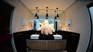 A modern bathroom with a curved vanity, black countertops, and a central floral arrangement. - Topazio Imperial Hotel (Itauna)