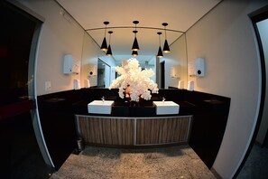 Une salle de bain moderne avec un meuble-lavabo aux lignes courbes, des plans de travail noirs et un arrangement floral central.