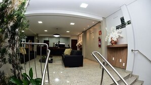 A lobby with a reception desk, a black sofa, and a staircase with metal railings. - Topazio Imperial Hotel (Itauna)