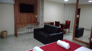 A hotel room with a bed, a sofa, a TV mounted on the wall, a desk, and a chair. - Topazio Imperial Hotel (Itauna)