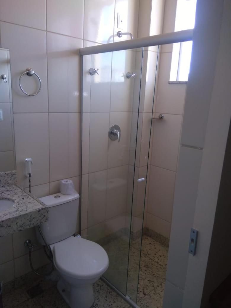 Casa de banho com sanita, chuveiro com divisória de vidro e lavatório de mármore.