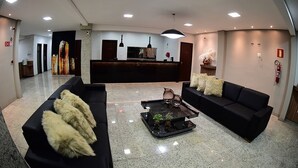 A modern lobby with two black sofas, a glass coffee table, and a reception desk. - Topazio Imperial Hotel (Itauna)