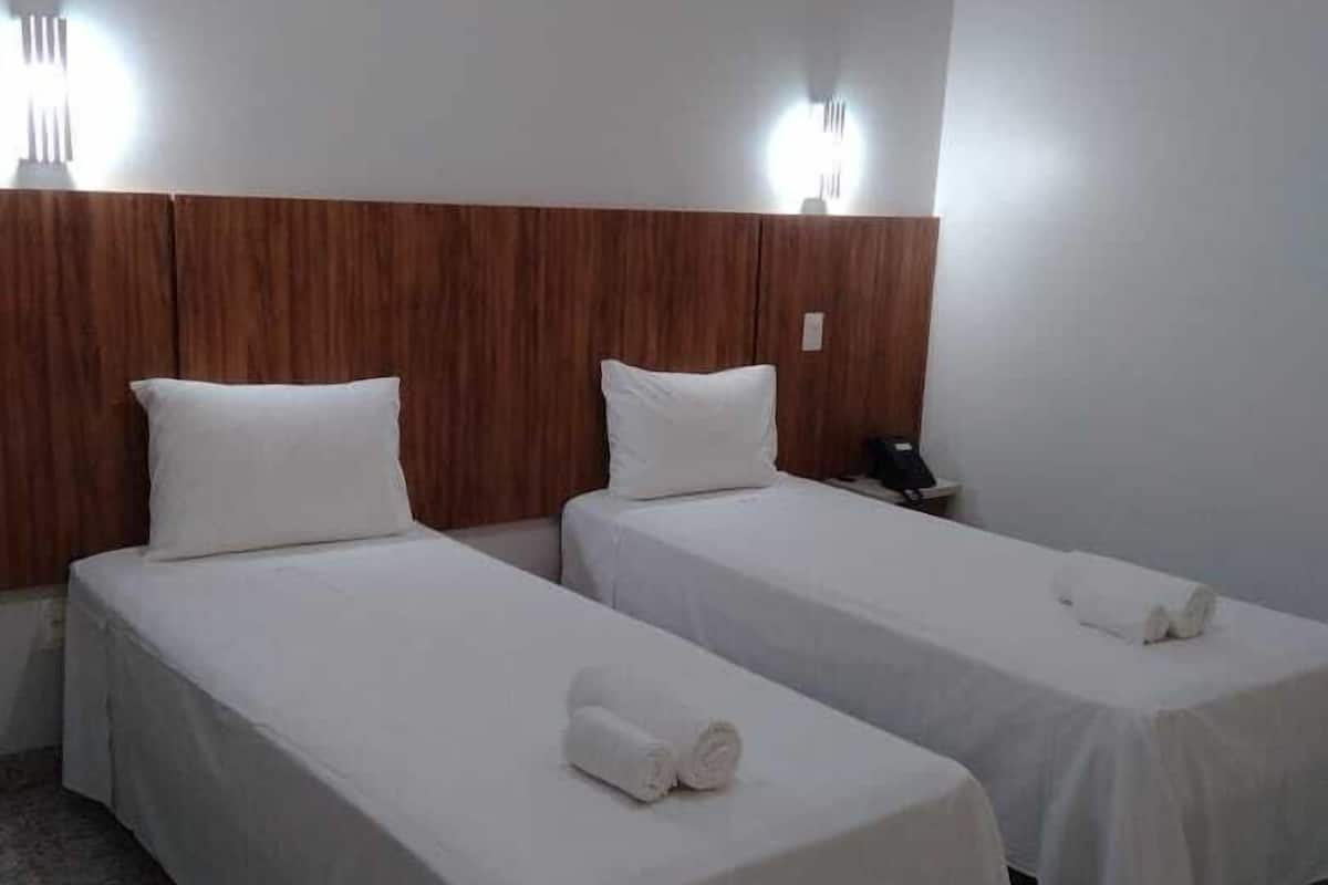 A hotel room with two single beds, wooden headboard, white bedding, and a phone on the nightstand.