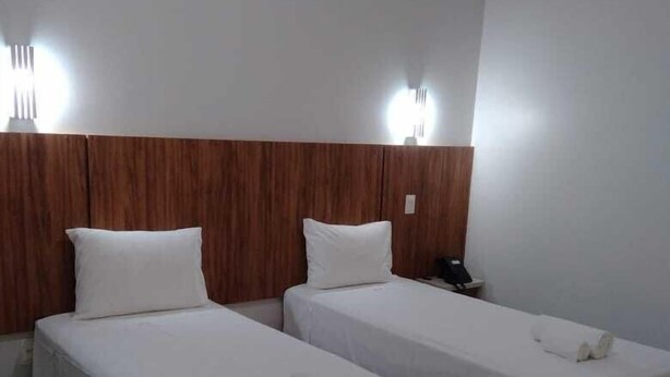 A hotel room with two single beds, wooden headboard, white bedding, and a phone on the nightstand. - Topazio Imperial Hotel (Itauna)