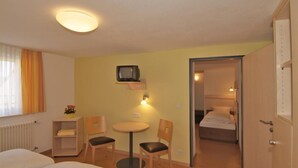 A hotel room with a bed, a desk, two chairs, a small table, a television, and a door leading to another room. - Hotel Haus am Berg (Trier)