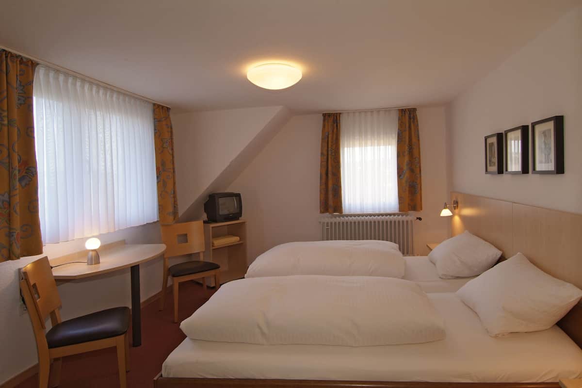 A hotel room with a bed, a desk, a chair, a television, and a radiator.