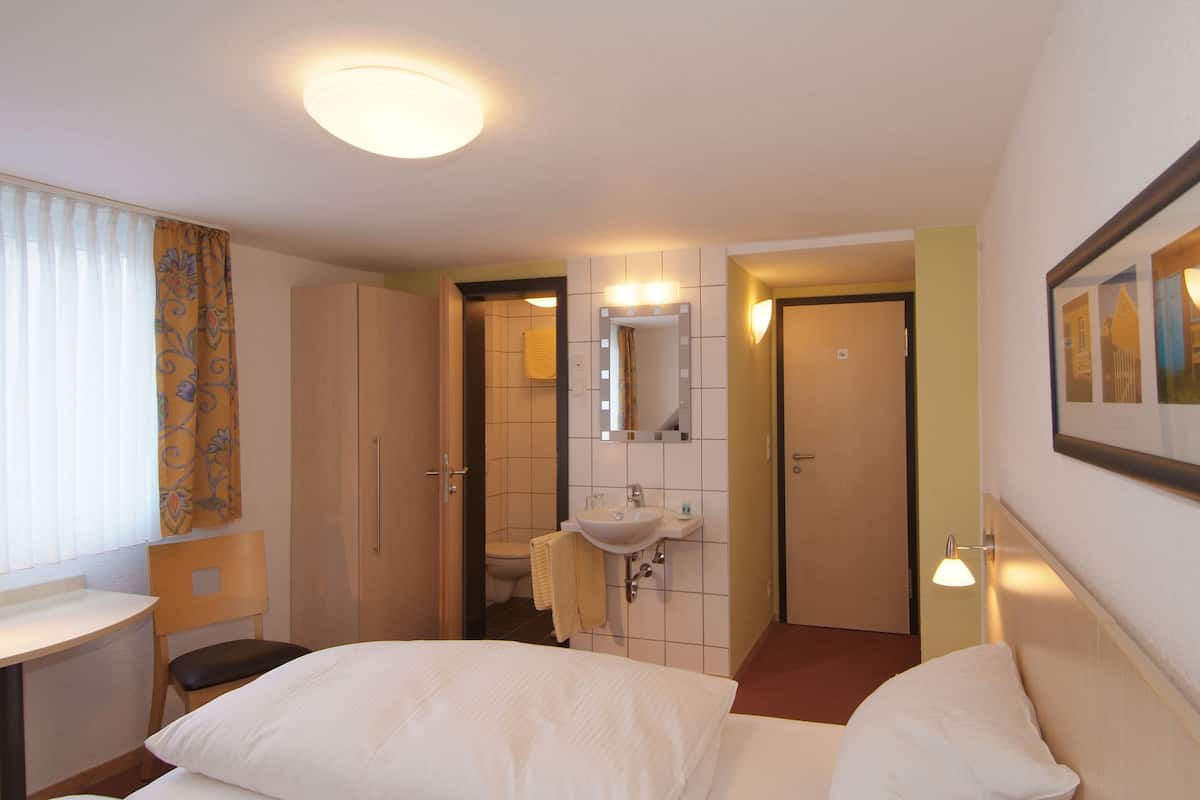 A hotel room with a bed, a desk, a bathroom with a sink and mirror, and a framed picture on the wall.