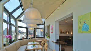 A modern dining area with a large window, a sofa, and several tables. - Hotel Haus am Berg (Trier)