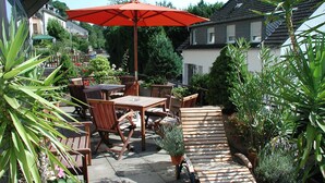 An outdoor patio with wooden furniture, a red umbrella, and potted plants. - Hotel Haus am Berg (Trier)