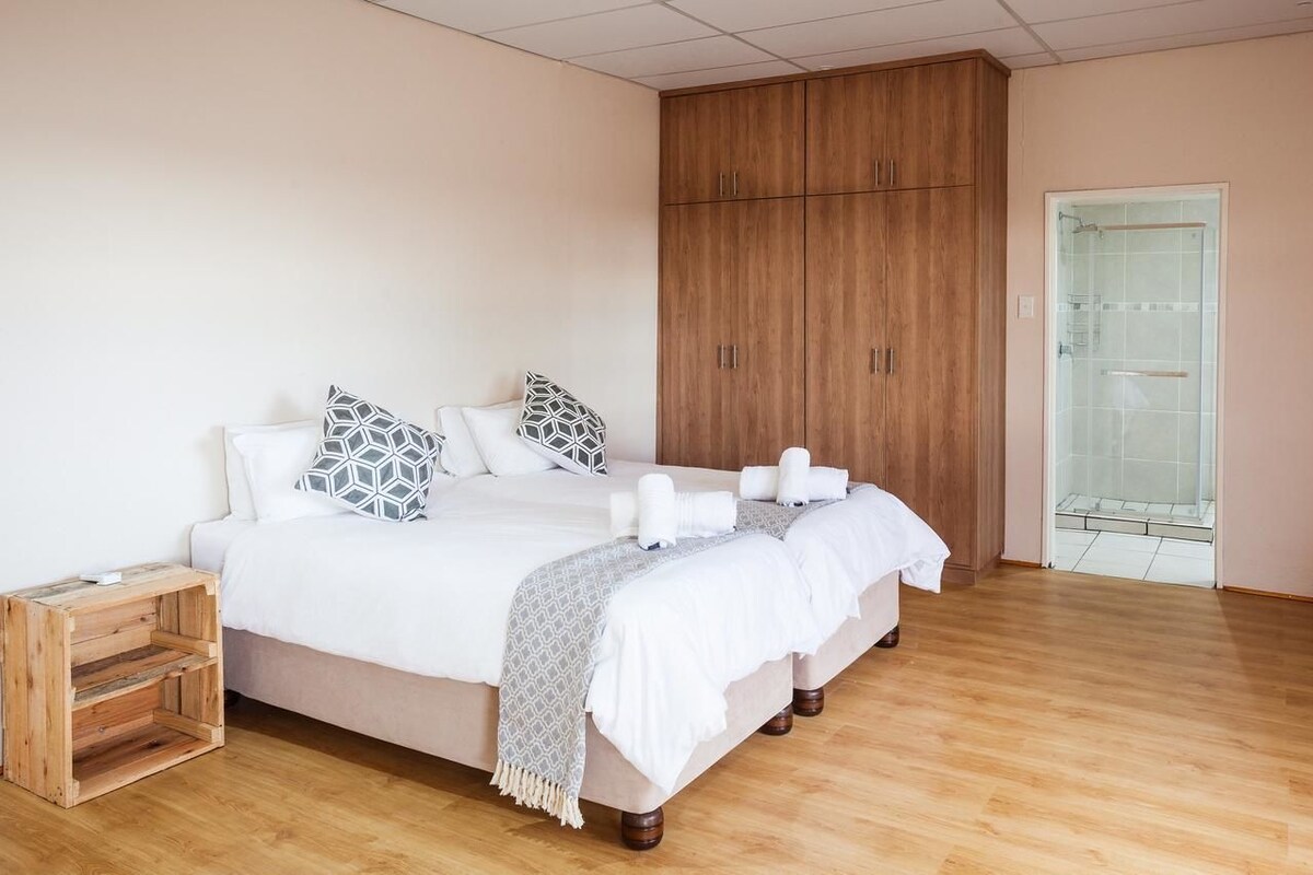 A double bed with two pillows, a wooden wardrobe, and a glass shower door.