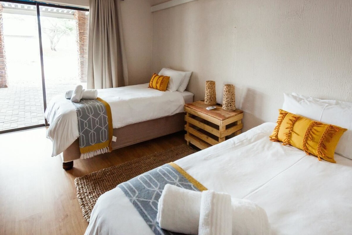 A hotel room with two beds, a wooden side table, and a large window.