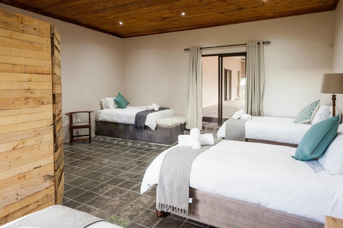 A hotel room with two beds, a wooden wall, a tiled floor, and a view through a glass door.