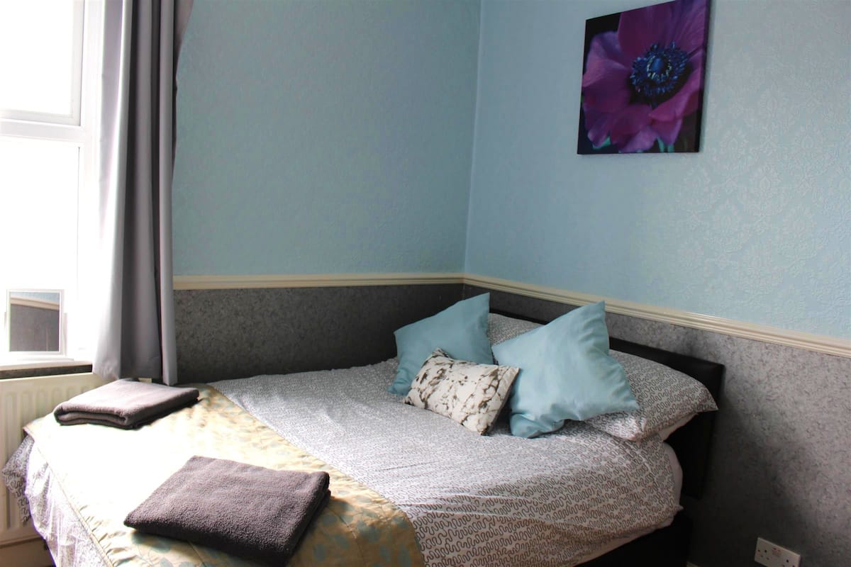 A neatly made bed with a patterned bedspread, two pillows, and folded towels.