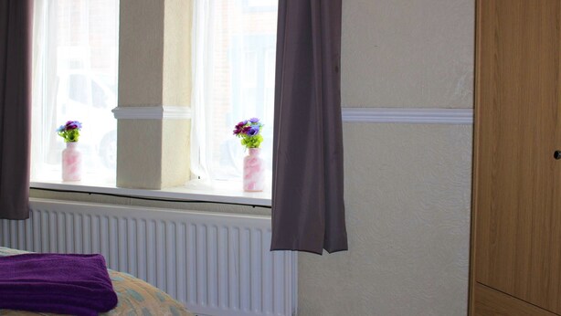 Een kamer met een raam, een radiator en een houten garderobe.