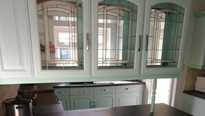 Een keuken met een zwart aanrecht, drie barkrukken en lichtgroene kasten met glazen deuren.
