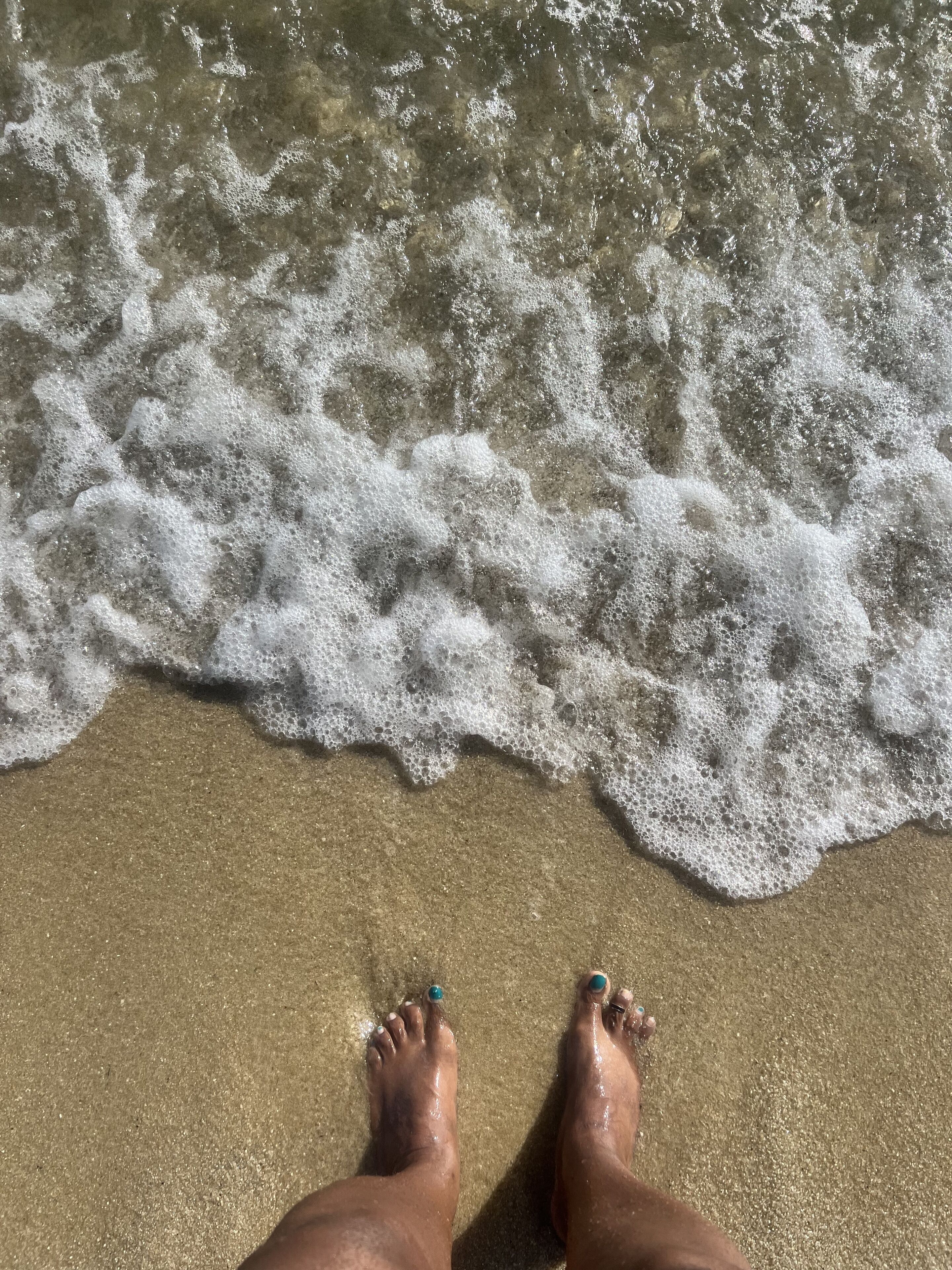 Piedi con smalto alle dita che si trovano su una spiaggia sabbiosa con le onde che si avvicinano.