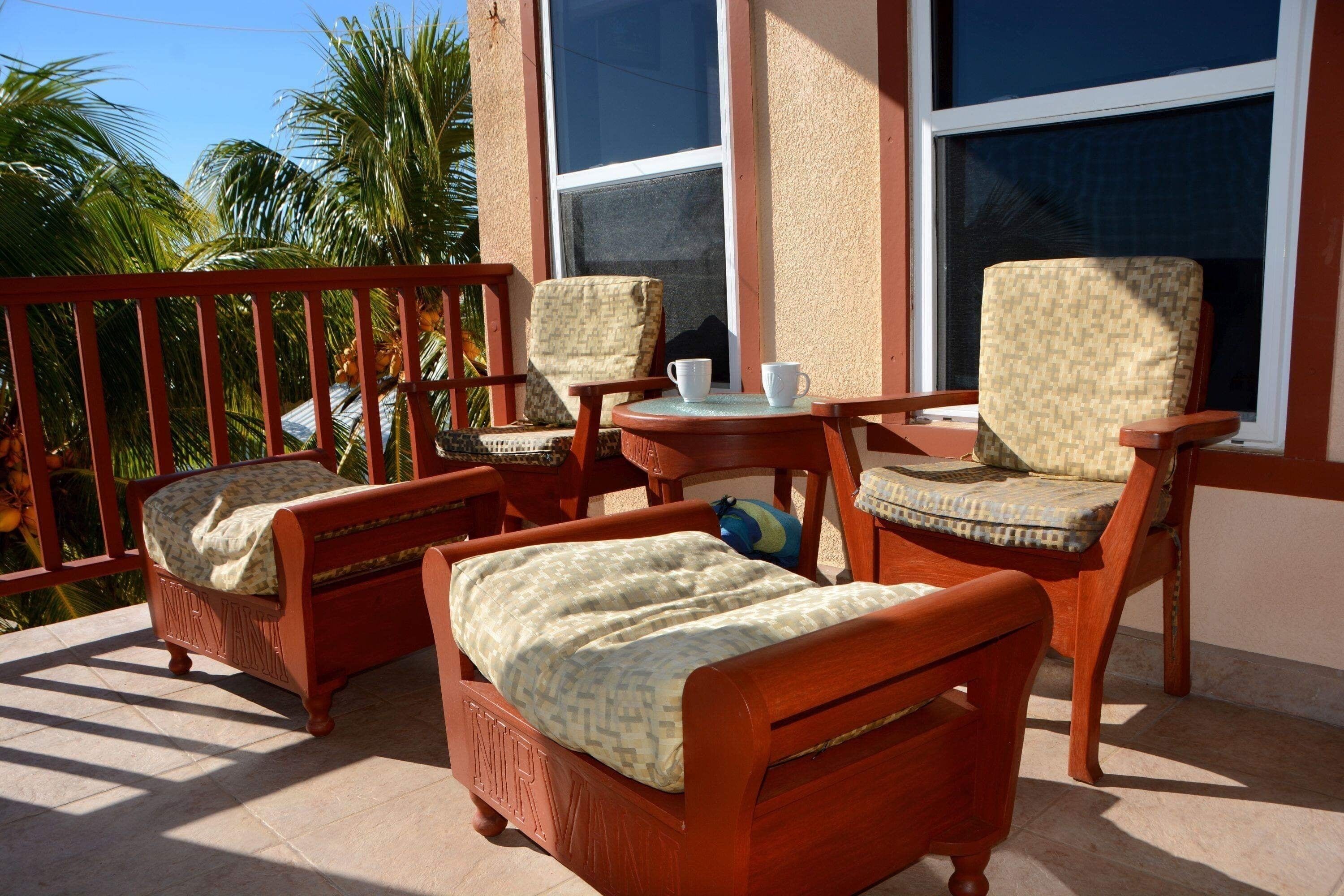 A balcony with two wooden chairs, a small table, and a bed with a patterned bedspread.