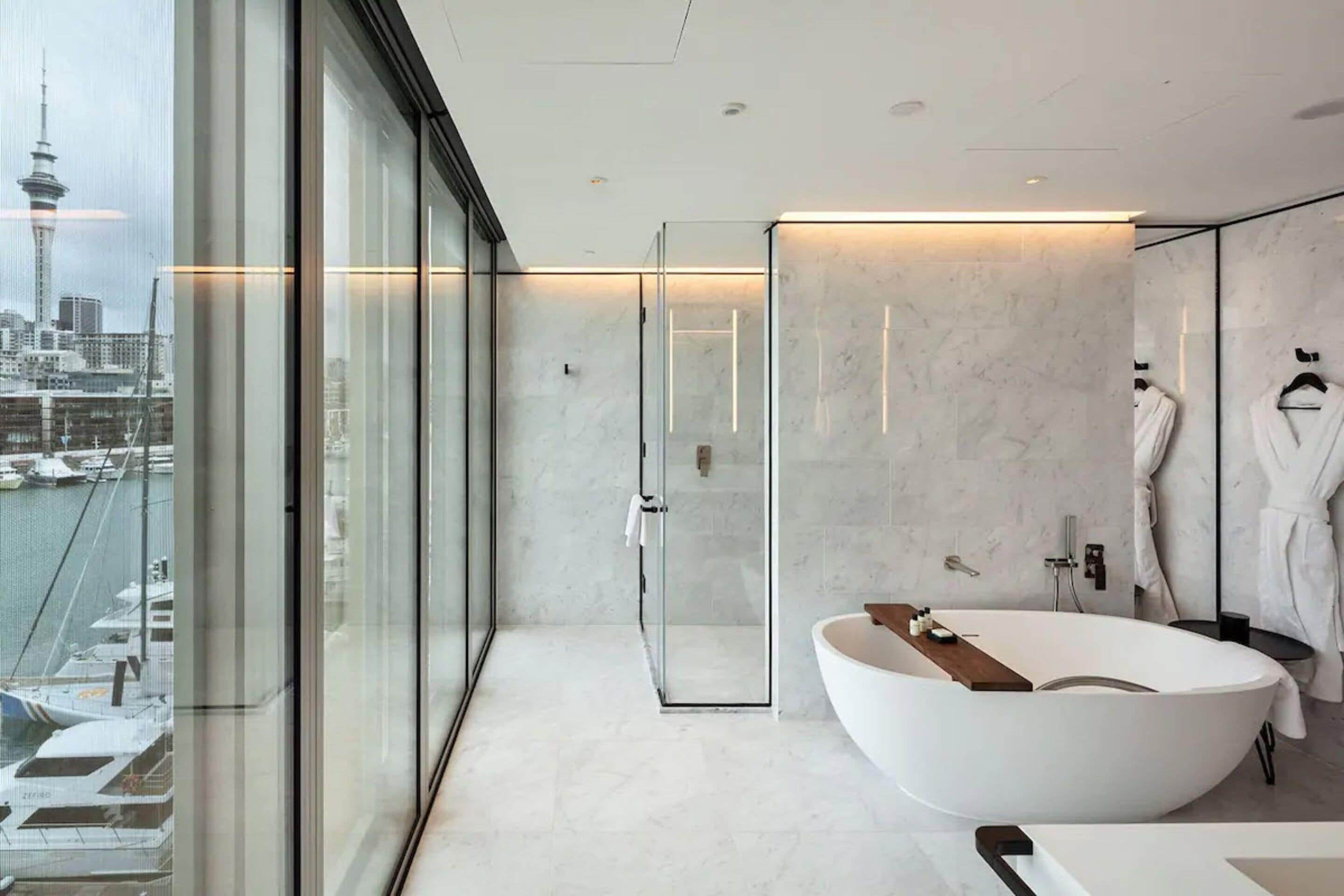 Un bagno moderno con una vasca freestanding, box doccia in vetro e vista sulla città attraverso ampie finestre.
