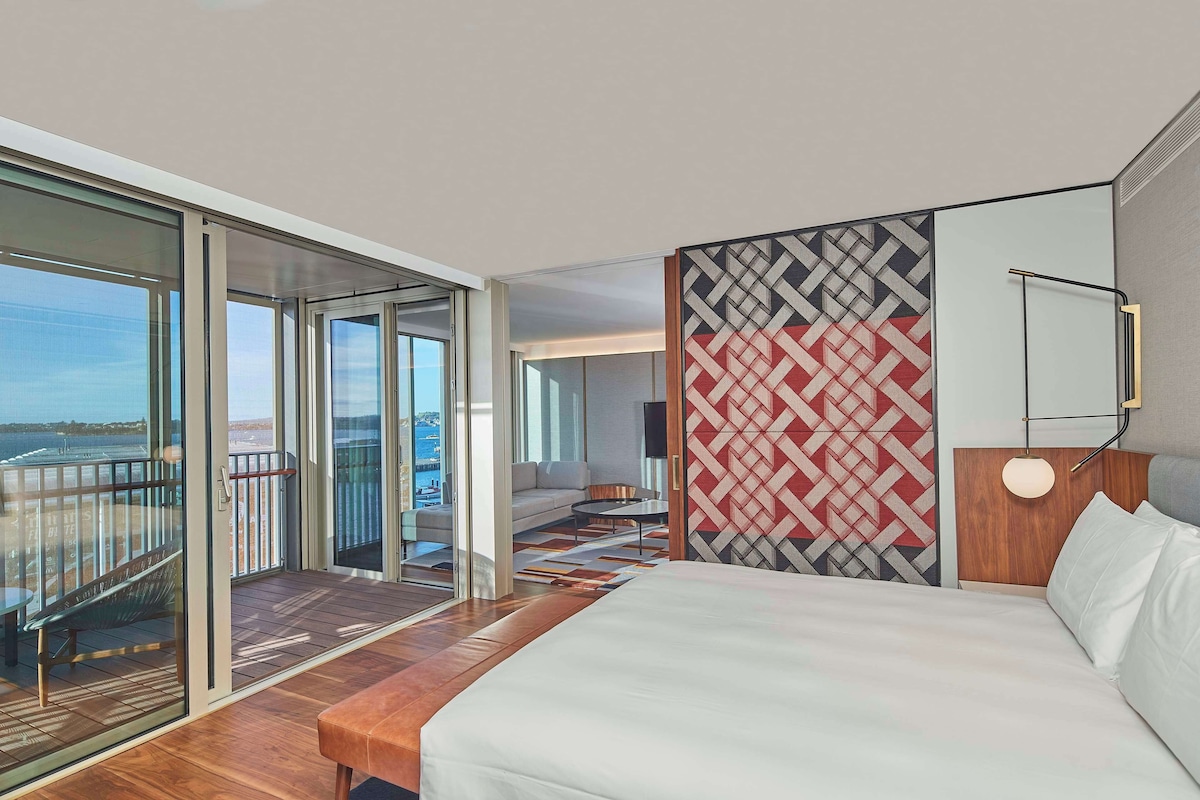 A modern hotel room with a large bed, a balcony with a view, and a patterned wall.