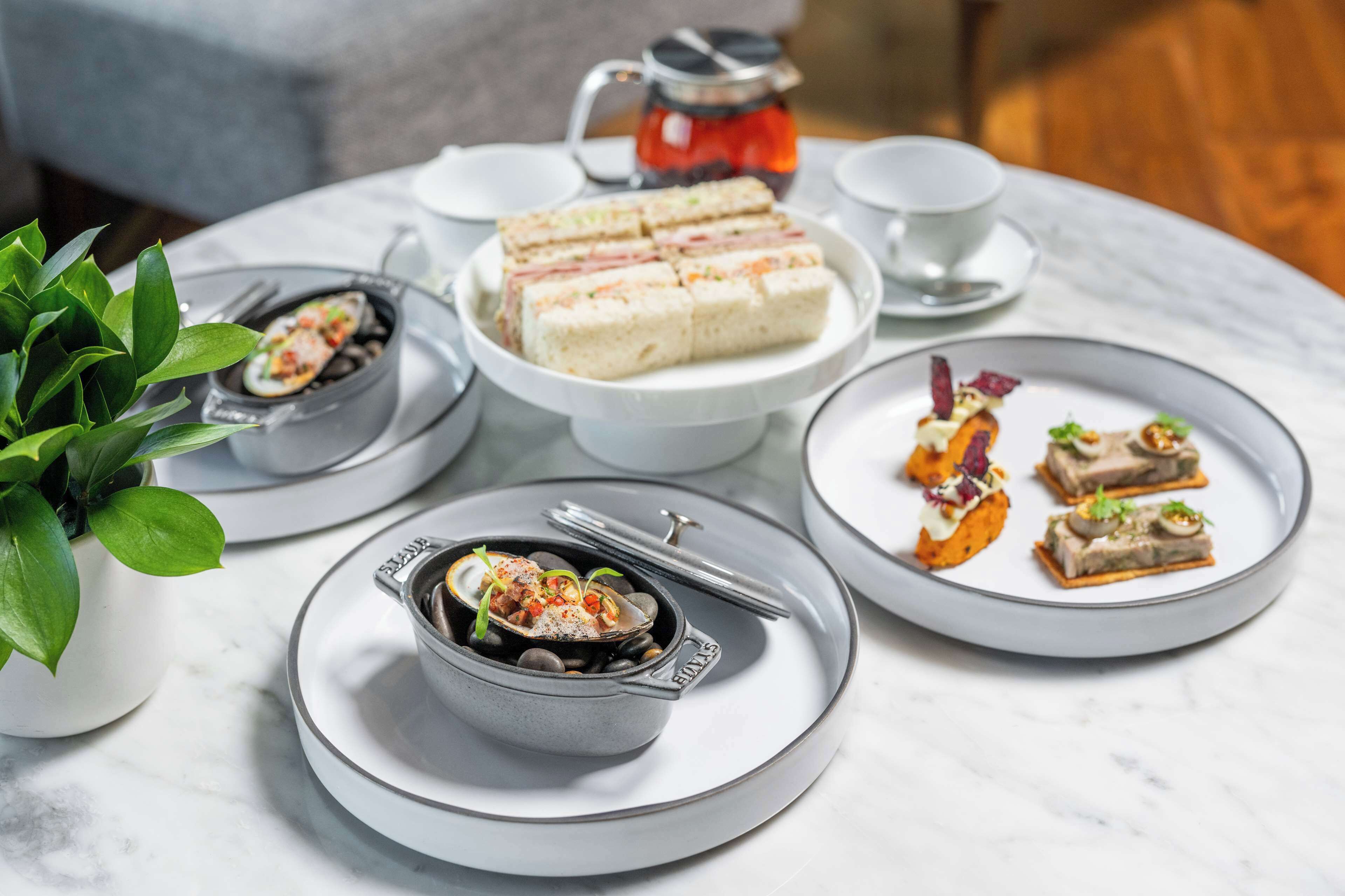 A table set with various dishes, including a bowl of soup, a plate of sandwiches, and several small plated desserts.