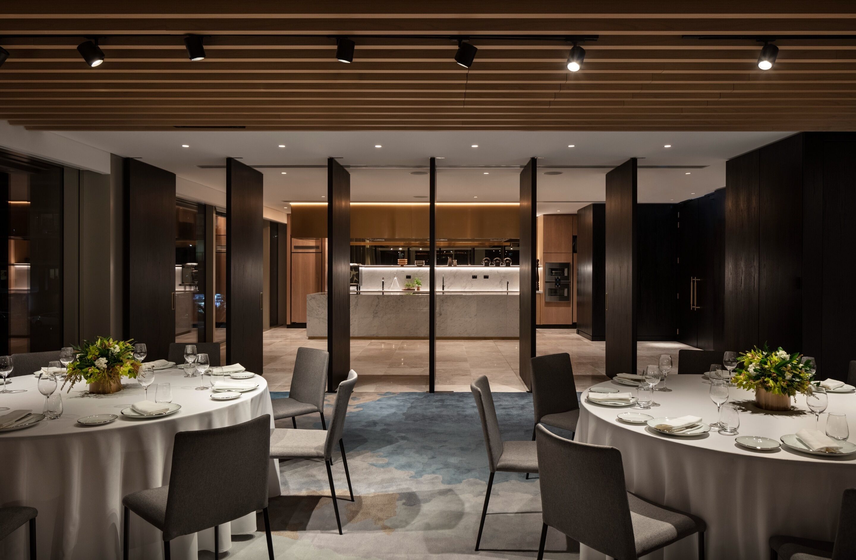 Un espace repas moderne avec des tables rondes, des chaises et un îlot central, la cuisine étant visible au fond.