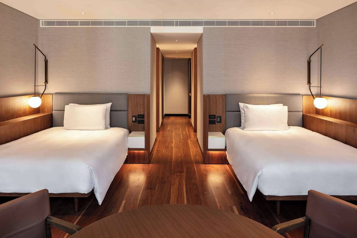 A hotel room with two beds, wooden flooring, and modern wall sconces.