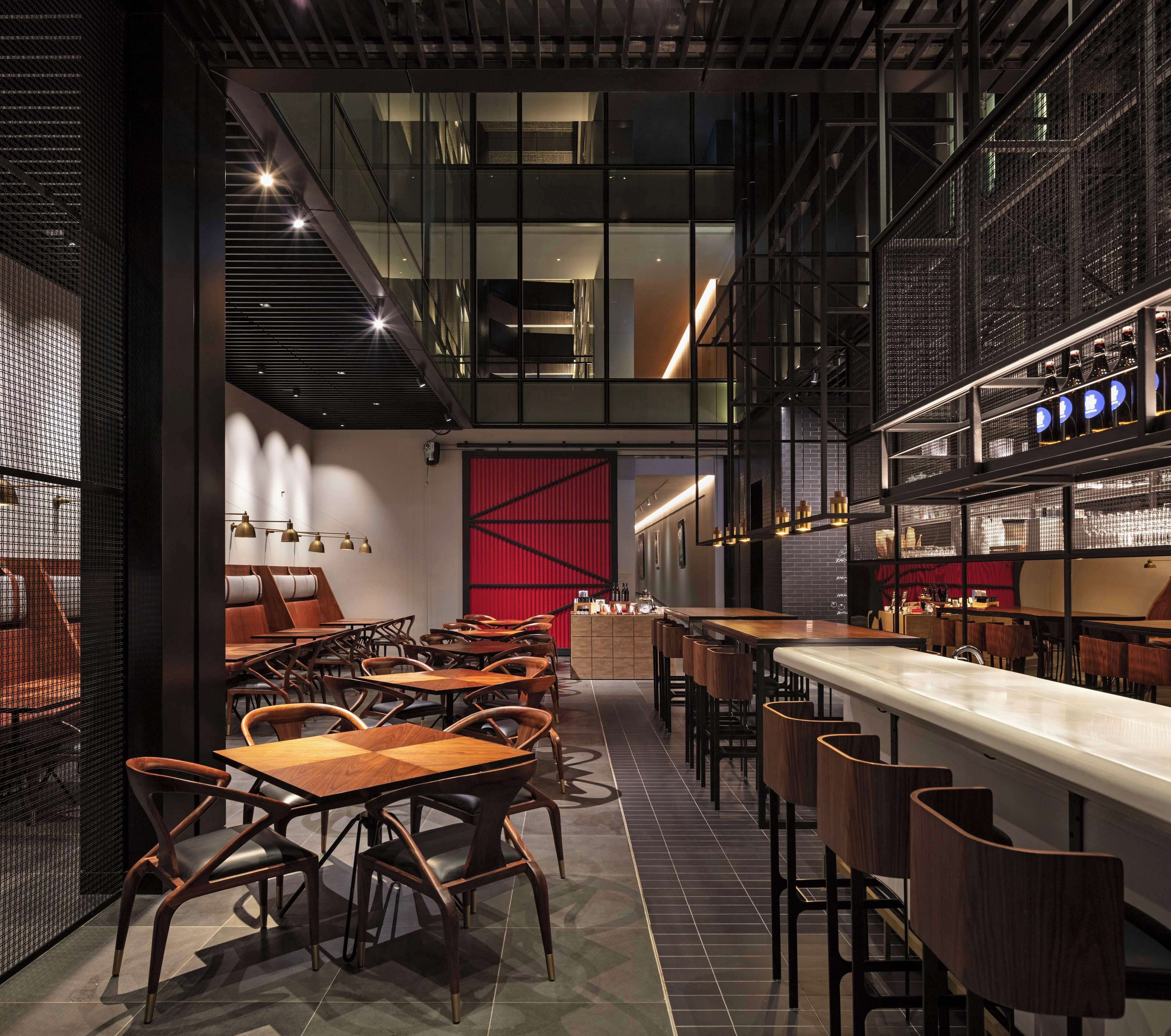 A modern restaurant with high ceilings, exposed ductwork, and a bar area with stools.