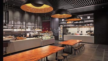 A modern cafe interior with wooden tables and bar seating, a coffee bar, and hanging pendant lights.