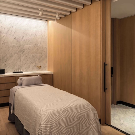 A modern bedroom with a bed, wooden wardrobe, marble wall, and a bathroom with a sink and mirror.