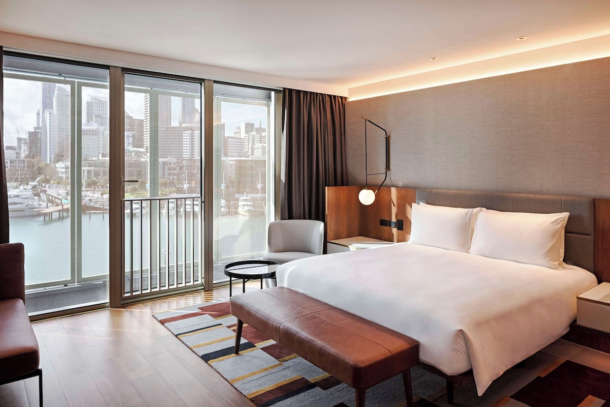 A modern hotel room with a large bed, a bench, a desk, and a chair.