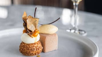 Ein Dessert auf einem weißen Teller, im Hintergrund ein Glas Weißwein.
