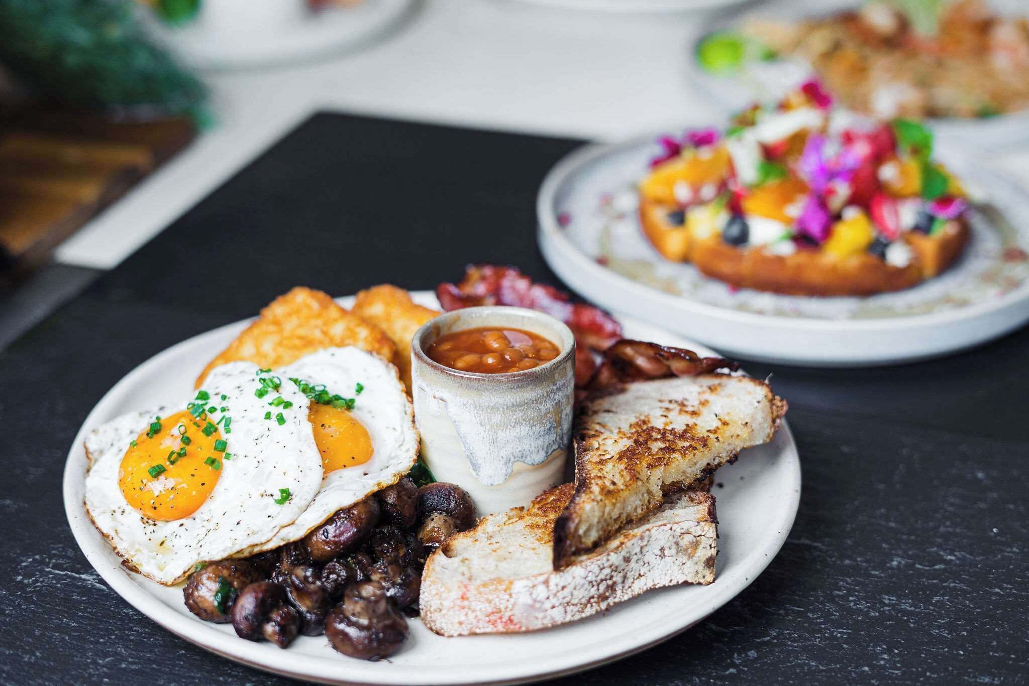 A breakfast plate with eggs, beans, toast, and a small cup of sauce.