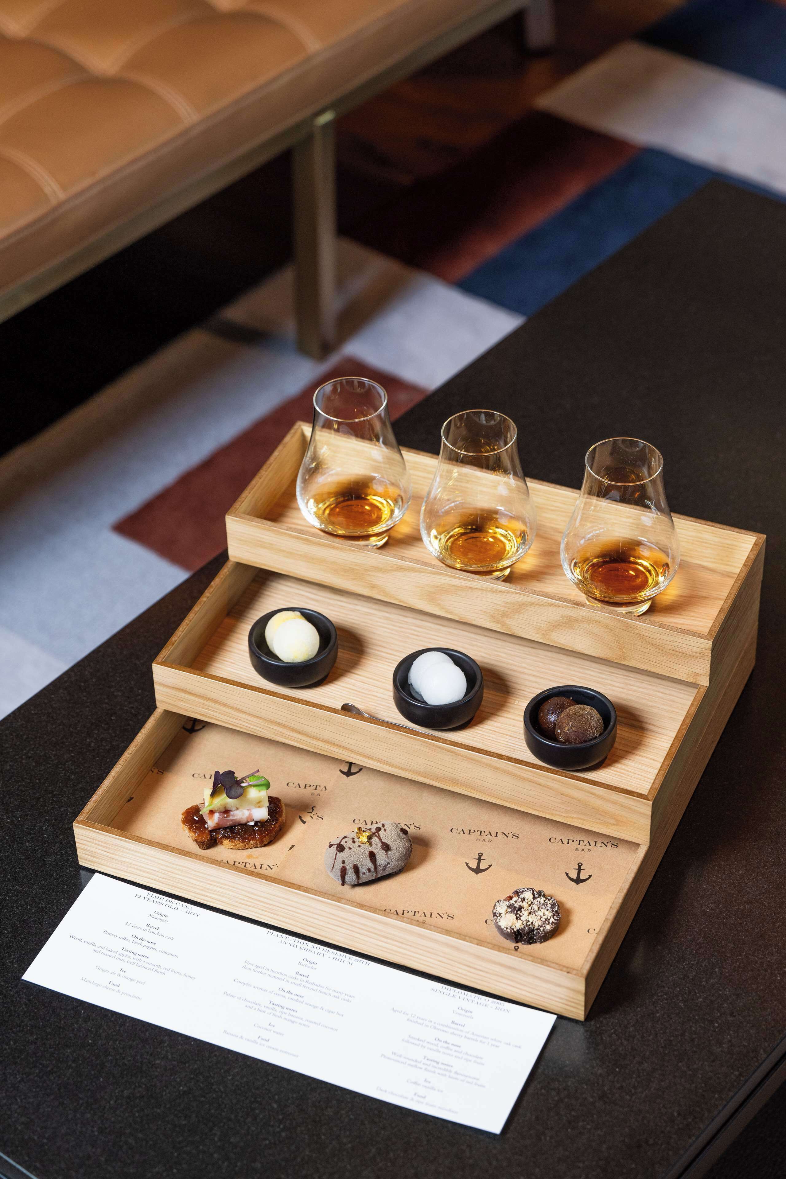 Una bandeja de madera con vasos de whisky y pequeños recipientes de condimentos.