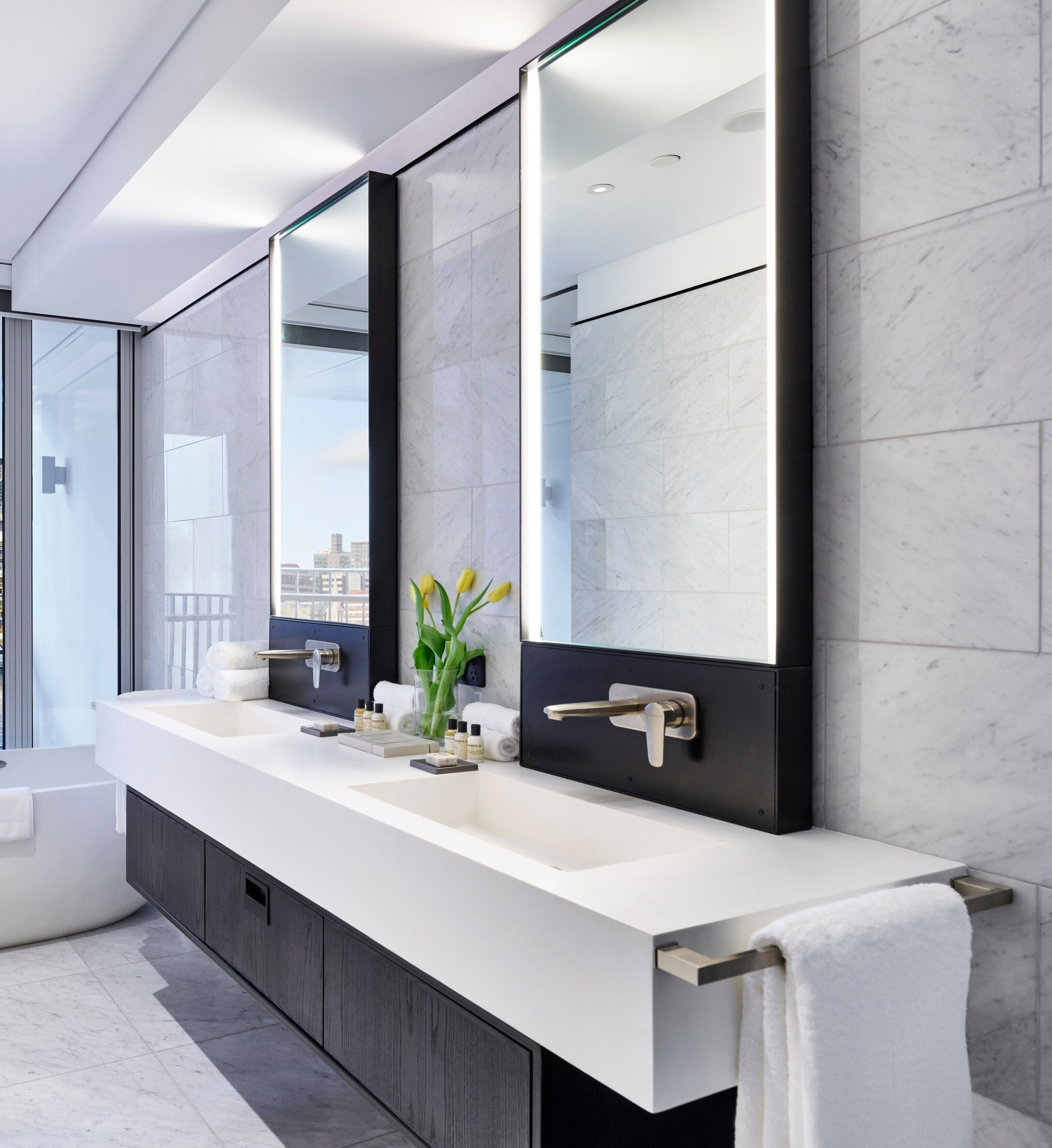 A modern bathroom with a large mirror, a bathtub, and a vanity with multiple sinks.