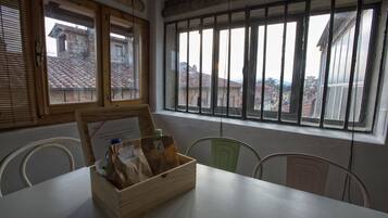 A room with a wooden table, a window with blinds, and a view of buildings outside.
