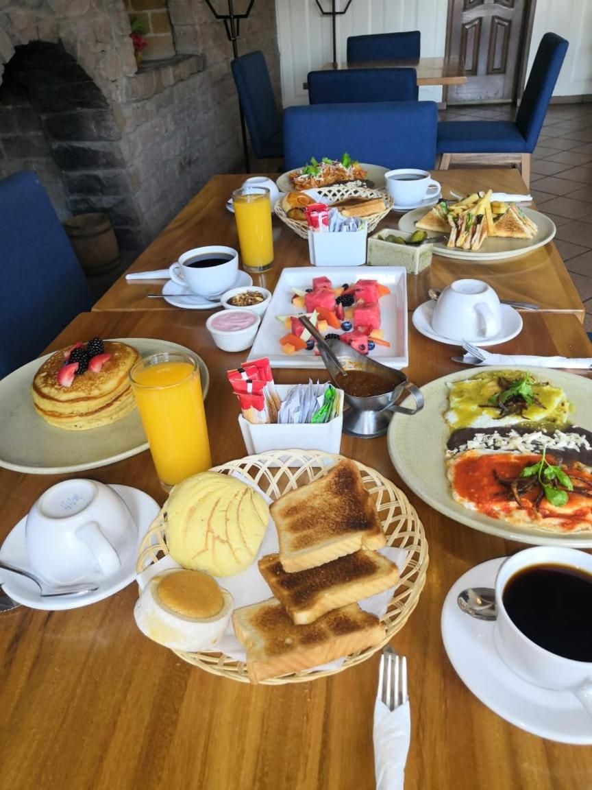 Un bufé de desayuno con diversos platos, entre ellos panqueques, tostadas y una variedad de frutas y verduras.