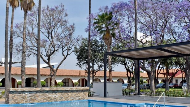 A swimming pool with clear blue water, surrounded by palm trees and a covered seating area. - Hotel Sand's San Luis Potosí (San Luis Potosi)