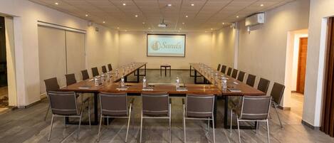 Uma sala de conferências com uma mesa comprida, cadeiras, uma tela de projetor e uma tela para apresentação.