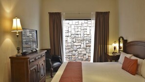 A hotel room with a bed, a desk with a lamp, a television, and a stone wall. - Hotel Sand's San Luis Potosí (San Luis Potosi)