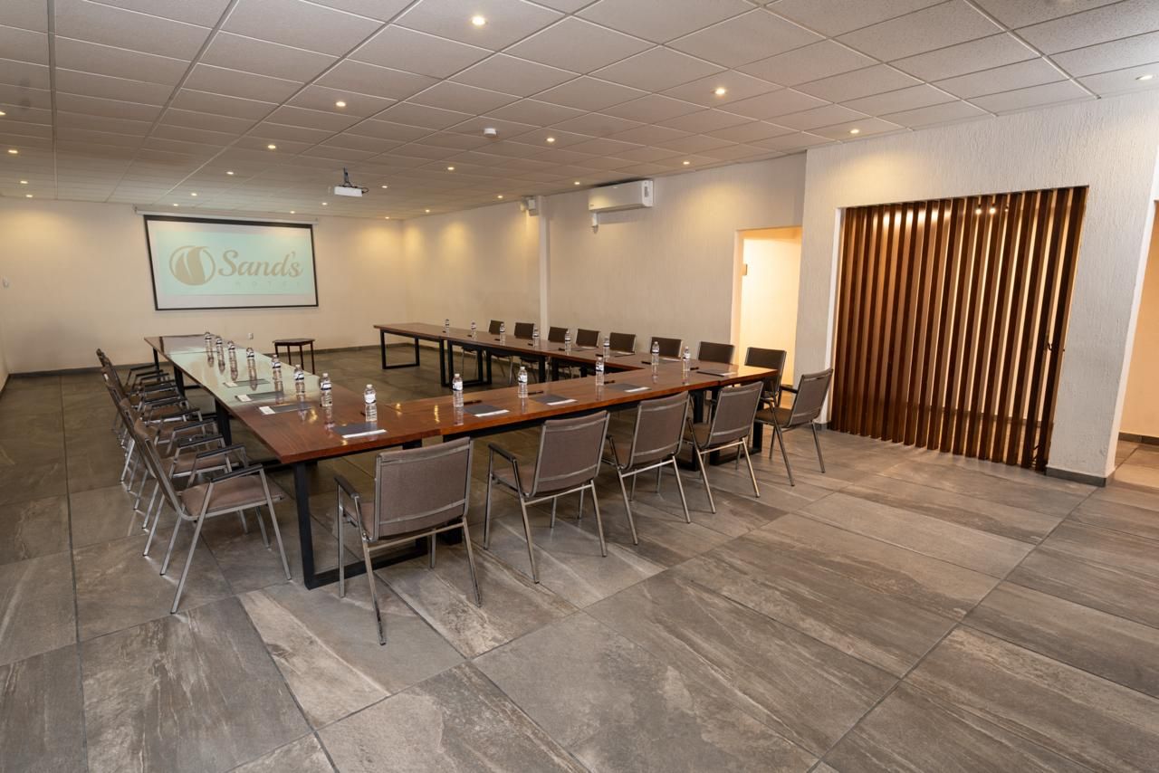 Un salón de conferencias con una mesa larga, sillas, una pantalla de proyector y una partición de madera.