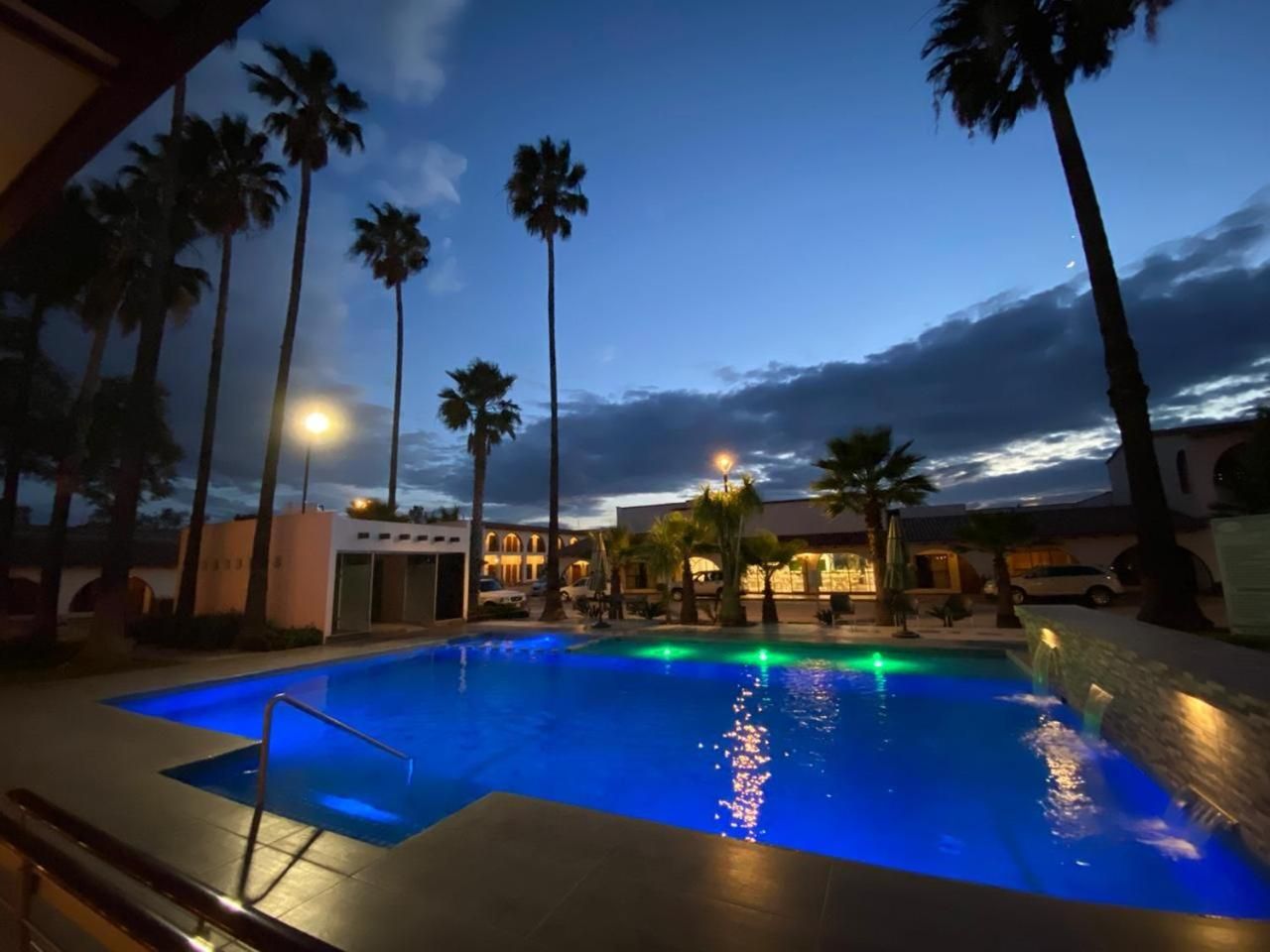 Une piscine avec vue sur un immeuble et des palmiers, au crépuscule.
