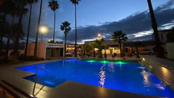 Une piscine avec vue sur un immeuble et des palmiers, au crépuscule.