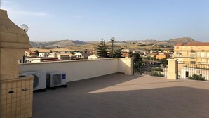 A rooftop terrace with air conditioning units, a view of a town and hills in the distance, and a clear sky. - Stella del Mare (Licata)